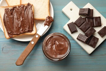 Tasty chocolate butter, pieces, knife and slices of bread on light blue wooden table, flat lay