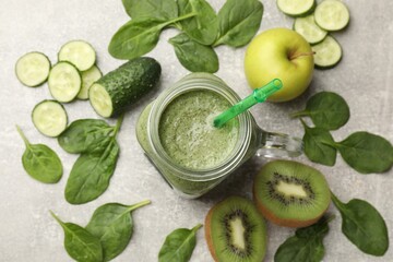 Tasty smoothie in mason jar, spinach leaves, apple, kiwi and cucumber on grey textured table, flat...