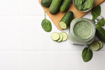 Tasty smoothie in mason jar, spinach leaves, lime and cucumber on white tiled table, flat lay....