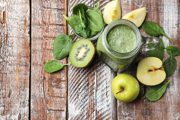 Tasty smoothie in mason jar, spinach leaves, apple and kiwi on color wooden table, flat lay