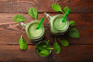 Tasty smoothie in mason jars and spinach leaves on wooden table, flat lay
