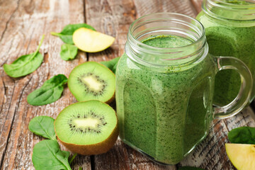 Tasty smoothie in mason jars, spinach leaves and kiwi on color wooden table, closeup