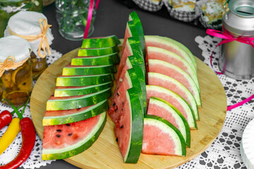 Sliced watermelon arranged on a wooden board, surrounded by rustic picnic elements like chili...