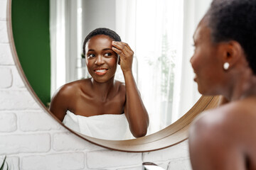 Woman applying skincare product in a well-lit bathroom while looking in a round mirror