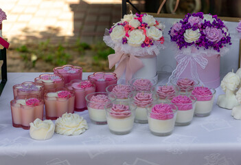 Handmade decorative candles shaped like roses displayed on a white tablecloth, next to floral gift boxes with pink, white, and purple flowers.