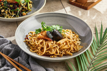 Seafood wok-fried noodles, bright overhead composition, garnished with cilantro, in ceramic bowl