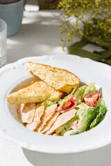 Caesar salad with grilled chicken in bright natural lighting, overhead composition, rustic white plate