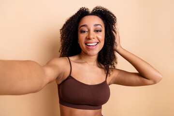 Portrait of a joyful young woman with curly hair posing in casual attire on a beige background radiating confidence