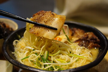 Close-up of Japanese Ramen Noodles with Pork Belly Lifted by Chopsticks