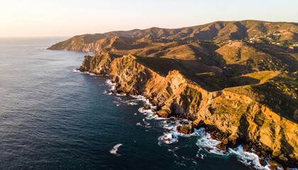 Fototapeta premium Aerial view of jagged cliffs meeting blue ocean under golden hour sunlight