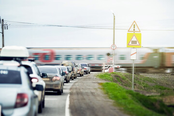 At a railway crossing in a suburban area, several cars are lined up in a queue, waiting for a train...