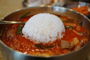 Close-up of Korean Spicy Pork Soup with a Whole Bowl of Steamed White Rice Flipped Onto the Top in a Brass Bowl