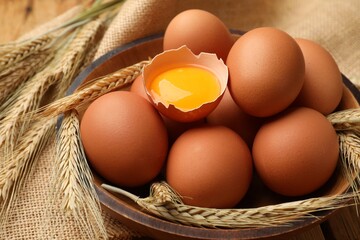 Fresh eggs, spikes and burlap cloth on wooden table, closeup