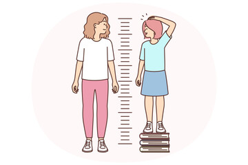 Little girl stands on books measuring growth and wants to compete with older sister © Valery