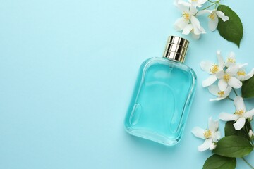 Bottle of perfume, beautiful jasmine flowers and green leaves on light blue background, flat lay....