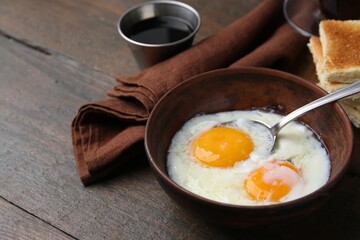 Traditional asian breakfast with half-boiled eggs in bowl, soy sauce and toasted bread on wooden table, closeup. Space for text