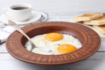 Half-boiled eggs in plate, spoon and toasted bread on white wooden table, closeup. Traditional asian breakfast