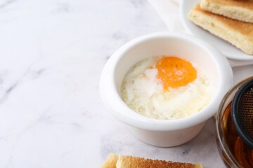 Half-boiled egg in bowl, tea and toasted bread on white marble table, closeup. Traditional asian breakfast