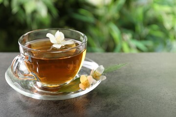 Aromatic jasmine tea in glass cup and flowers on grey table outdoors, closeup. Space for text