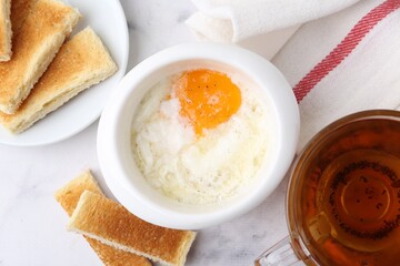 Half-boiled egg in bowl, tea and toasted bread on white marble table, flat lay. Traditional asian...