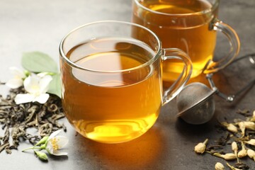 Aromatic jasmine tea in glass cups, brew and flowers on grey table, closeup