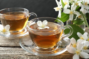 Aromatic jasmine tea in glass cups, flowers and green leaves on wooden table, closeup