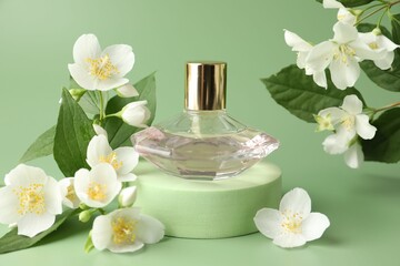 Bottle of perfume and jasmine flowers on green background, closeup