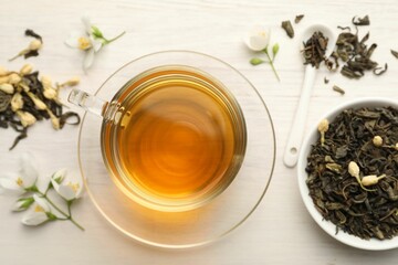 Tasty jasmine tea in cup, dry leaves and flowers on white wooden table, flat lay