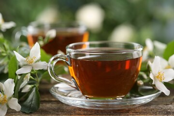 Tasty jasmine tea in cups and flowers on wooden table, closeup