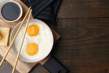 Traditional asian breakfast with half-boiled eggs in bowl, soy sauce, bread and chopsticks on wooden table, top view. Space for text