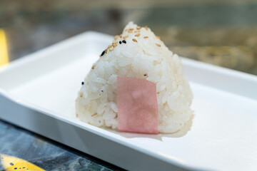 Close-up of pink and white salmon onigiri placed on a rectangular white plate with blurred background, macro shot with selective focus and copy space