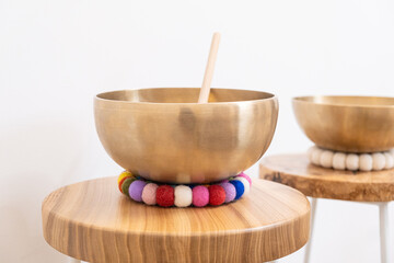 Singing bowl placed on a wooden stool with a colorful felt ball mat. The bowl, used for sound...