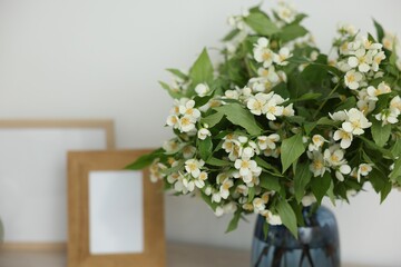 Beautiful jasmine flowers in vase and photo frames on table indoors, closeup. Space for text