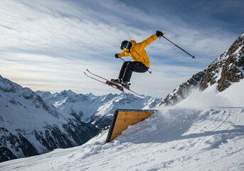 A skier captured mid-jump off a snowy ramp in the mountains