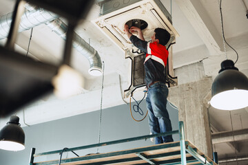 Technician performs installation work on ceiling-mounted air conditioning unit in modern office
