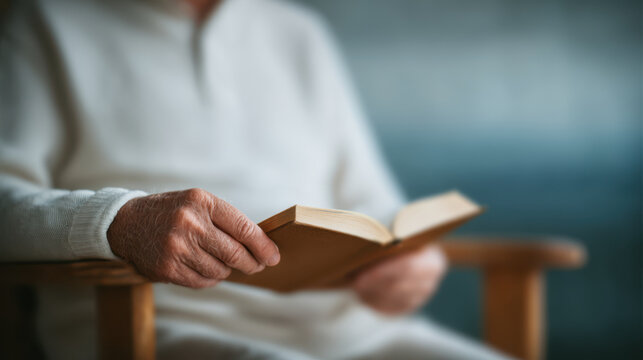 Elderly person reading book with focus on hand holding pages, cozy atmosphere with soft lighting and calm background