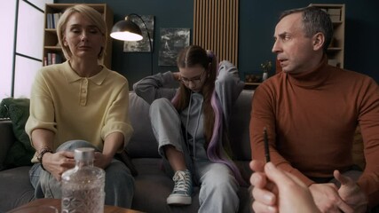 Slowmo of teen Caucasian girl putting on hood and covering her face avoiding conversation with her parents and unrecognizable psychologist during family counseling session in modern office