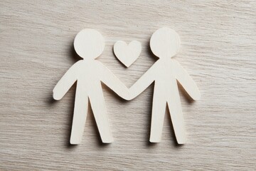 Two papercut figures holding hands with a heart above on a wooden surface