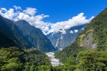 Obraz premium Lush green valley with a river flowing through mountainous terrain