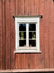 An old red plank wooden cottage. Finland. Red wood surface, weathered. White window