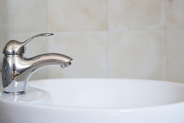 A sleek chrome faucet is positioned above a white ceramic basin in a contemporary bathroom. The clean lines highlight the simplicity and elegance of modern interior design.