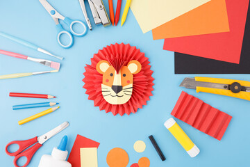 Color paper lion craft with red mane, glue and scissors on blue background, ideal for childhood...