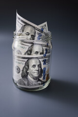 Hundred American dollars banknotes are stored in glass jar, emergency reserve or saving money for rainy day concept. Close-up