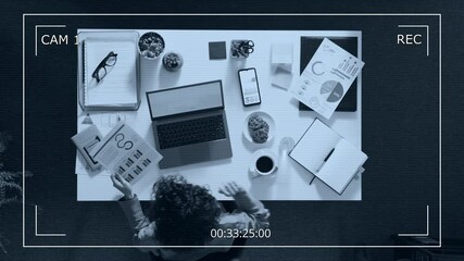Security camera video from above of female entrepreneur working on financial report at white desk with laptop, documents, open notebook, cup of coffee and cookies - Powered by Adobe