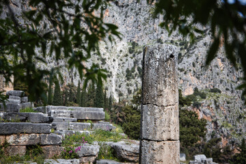 The gray ruins of ancient Delphi sit quietly under a partly cloudy sky, showing signs of age and history.