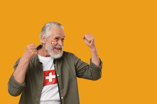 Excited fan with flags of Switzerland on his face and t-shirt against orange background. Space for text - Powered by Adobe
