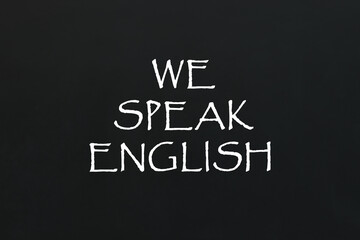 Fototapeta premium We Speak English inscription on black chalkboard. Language course