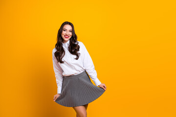 Young woman in white shirt and gray skirt posing joyfully against a vibrant yellow background...