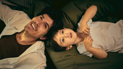 A father and son bond on a bed, enjoying quality time together in a warm home setting. Concept of family connection, candid moments and authenticity
