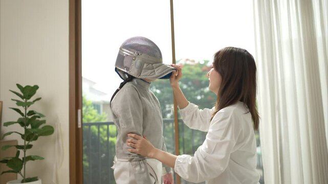 A girl in fencing gear with their mother preparing sports equipment before practicing fencing in preparation for the upcoming competition day